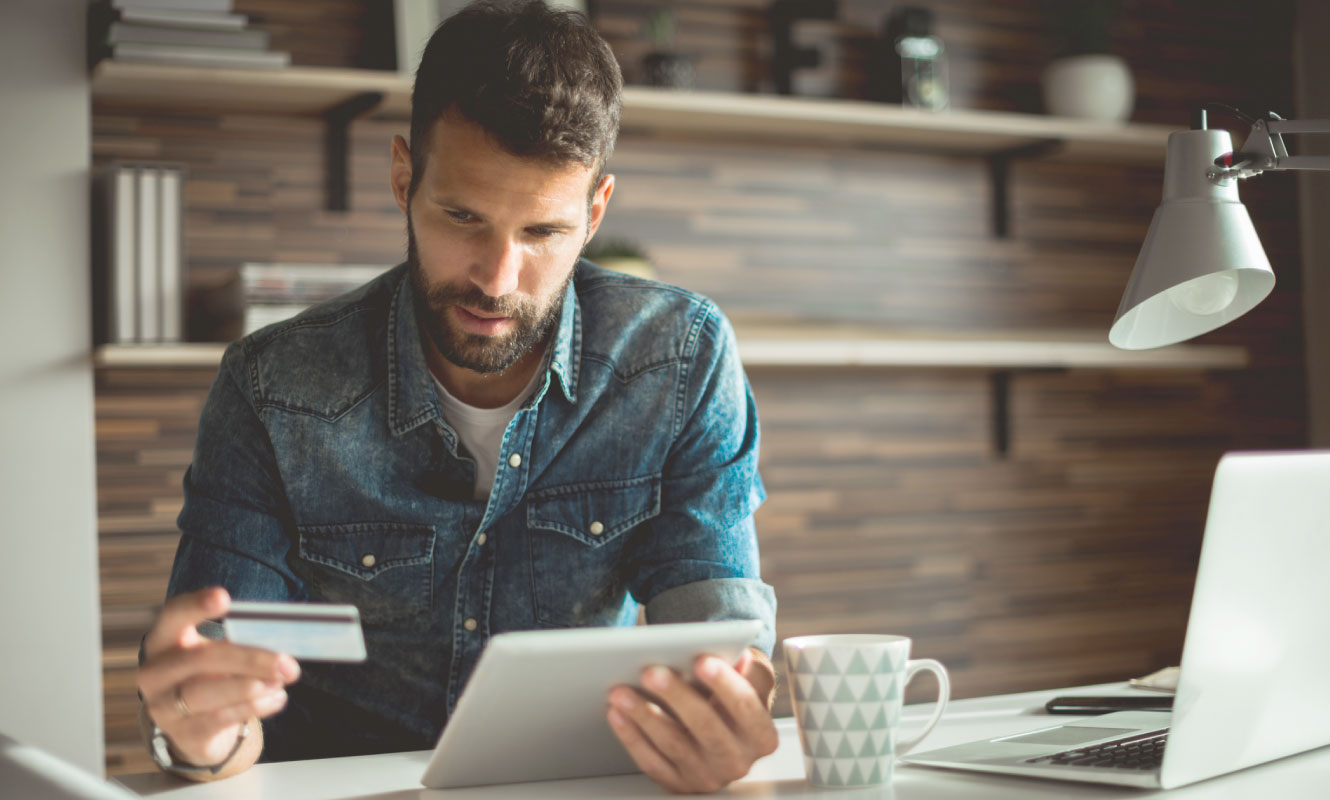 man sitting at a desk using his credit card and tablet 